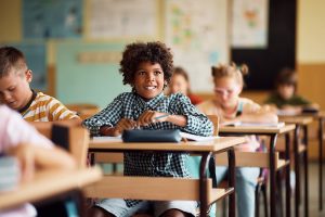 Estudante negro feliz frequentando uma aula no ensino fundamental, mostrando a importância da limpeza de escolas