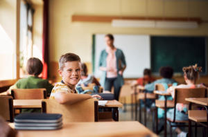 aluno olhando para a camera enquanto a professora ensina em escolas, classe cheia