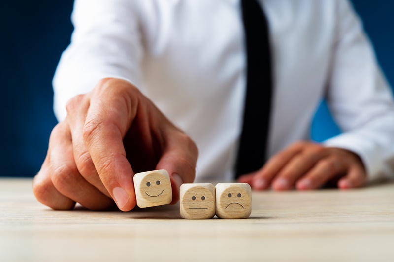 Closeup de um homem escolhendo dados de madeira com rosto sorridente de três opções (feliz, médio e triste) em uma imagem conceitual de satisfação do cliente por meio da nps divulgada pela rl higiene