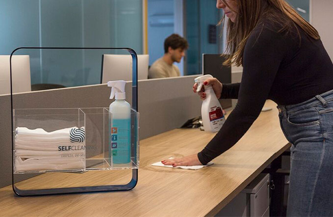 selfcleaning da rl higiene que trás limpeza para empresas. na foto uma mulher limpa uma mesa, estação de trabalho enquanto um homem faz seu serviço no fundo