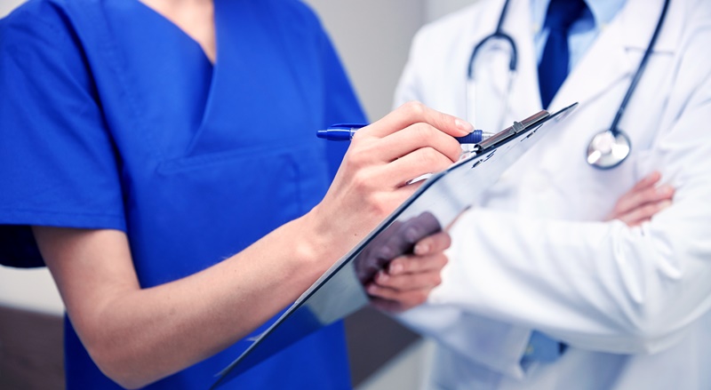 dois médicos lado a lado, um usando jaleco branco e outra jaleca azul fazendo anotações
