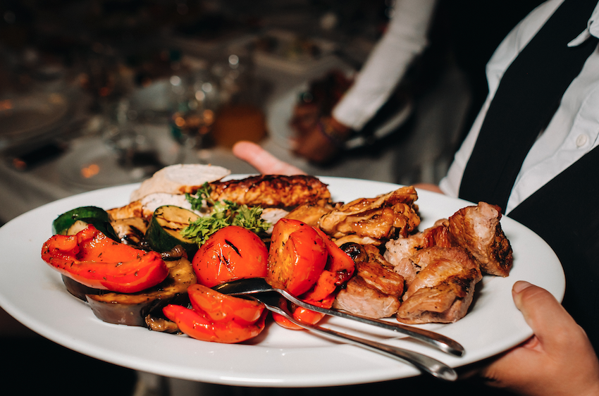 restaurante serve um prato quente de churrasco com legumes, carne frita, frango, garçom segura prato
